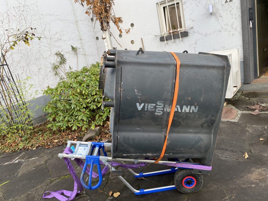 Das Bild zeigt, wie ein großer Tank mit Hilfe von Gurten an der Sackkarre befestigt wird.