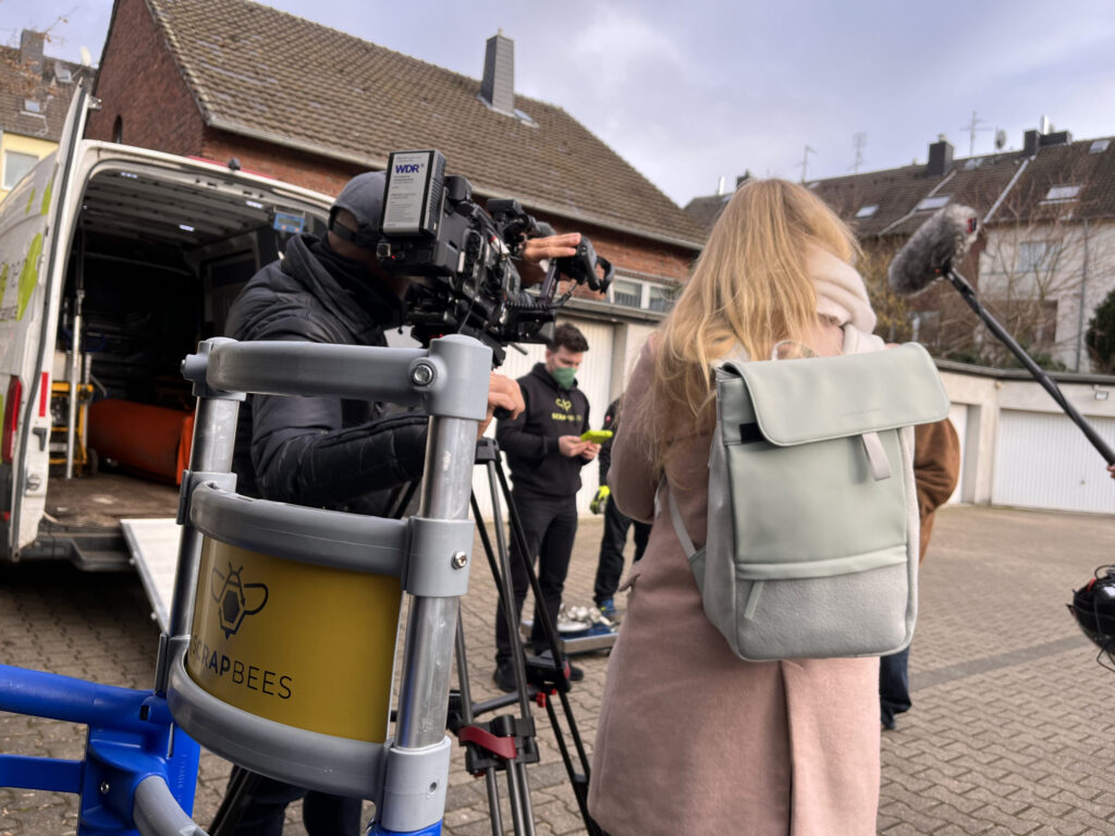 Das Bild zeigt, wie die Abholung vom Kamerateam und der Redakteurin begleitet wird.
