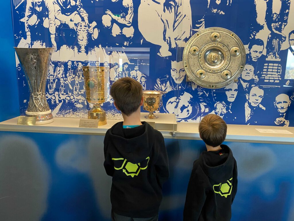Das Bild zeigt den SchrottBienen-Nachwuchs vor der Pokalvitrine im Schalke-Museum.