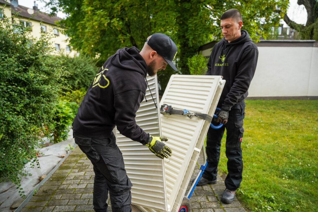Das Bild zeigt zwei Mitarbeiter der SchrottBienen beim Abtransport zweier Heizkörper.