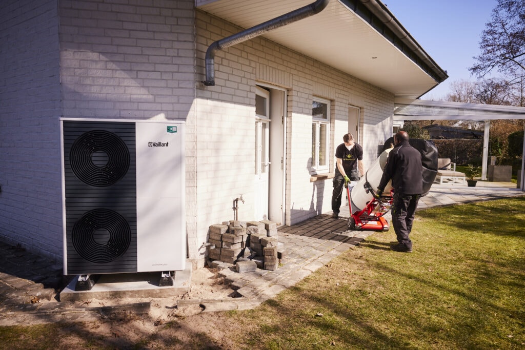 Das Bild zeigt zwei Mitarbeiter der SchrottBienen, wie sie mit Hilfe eines Treppenlifts einen Hezkessel abtransportieren. Im Vordergrund ist eine Wärmepumpe des Herstellers Vaillant zu sehen.