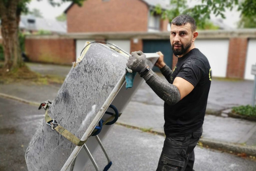 Das Bild zeigt einen Fahrer der SchrottBienen (Tarek), der eine alte Badewanne per Sackkarre Richtung Crafter zieht.